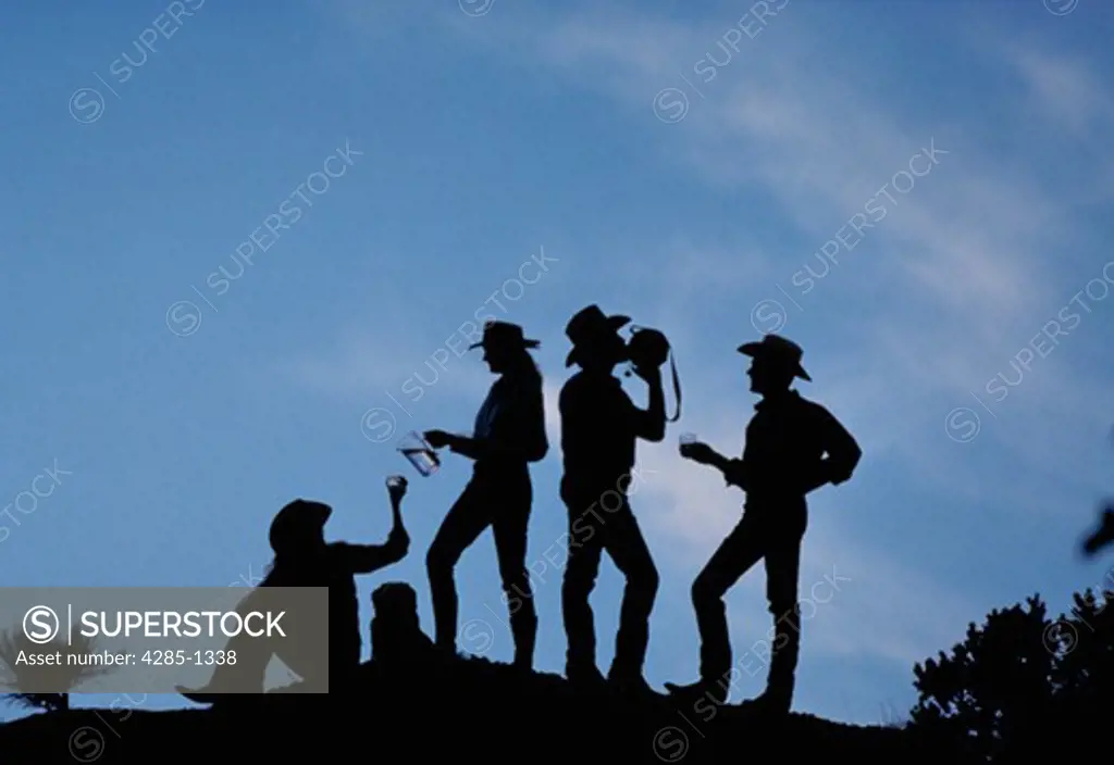 Silhouette of group of cowboys drinking from canteens against blue sky.