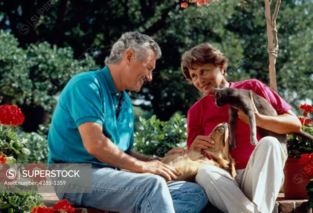 Senior couple sitting outside with pet dog and cat.