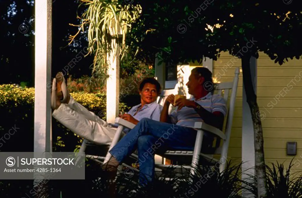 Retired couple sitting in rocking chairs on front porch.