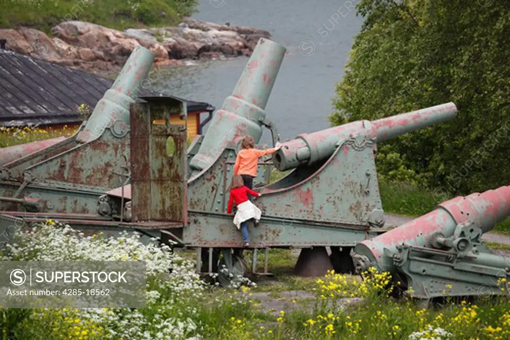 Finland, Helsinki, Helsingfors, Suomenlinna Island, Kustaanmiekka, Children Playing at Historic Cannon, Wild Flowers