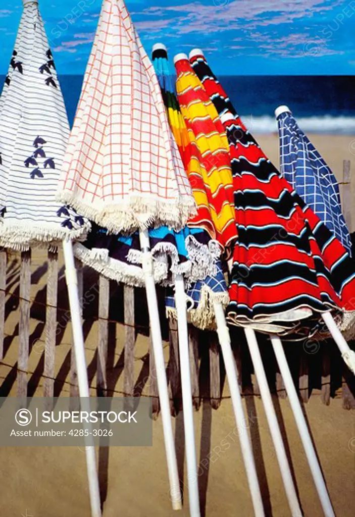 Colorful beach umbrellas laying against a fence.