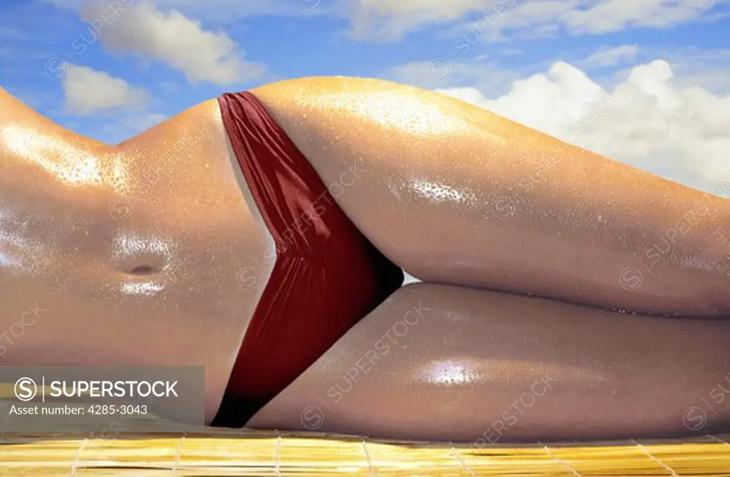 Girl torso, glistening wet, in dark red bikini bottom, laying on side and  on straw mat with blue sky and puffy clouds. - SuperStock