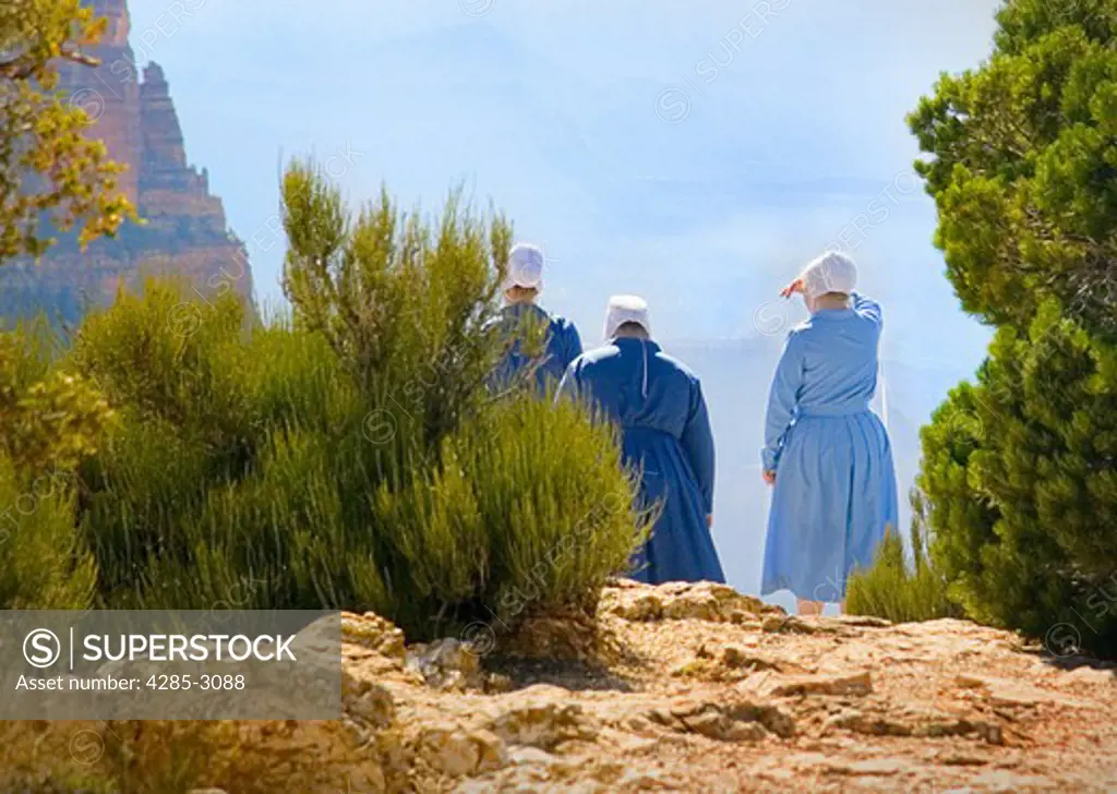 Amish girls in traditional blue dress and white hats overlooking the Grand Canyon on ledge with metal banister. (2)