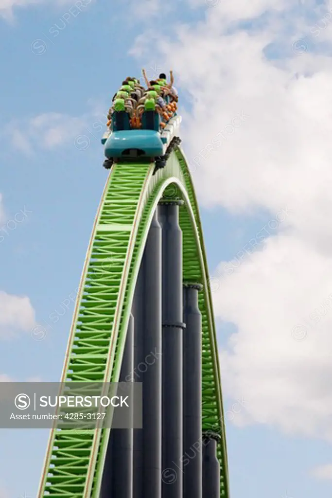 Roller coaster car on top of track with people raising arms and blue sky in background.