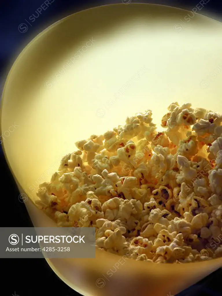 Popcorn in yellow bucket close-up with dramatic lighting.