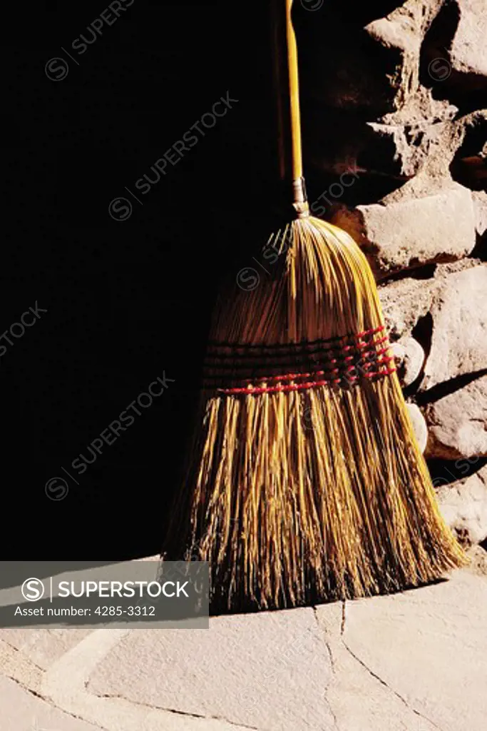 Old fashioned straw broom leaning against rock column, strong side light.