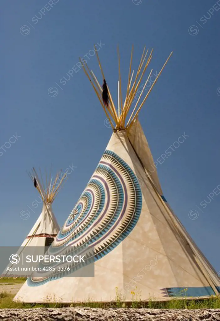 Two Indian teepees in a field with blue sky.