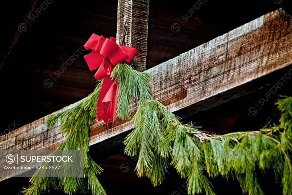 CHRISTMAS BOW AND GREEN GARLANDS HANGING FROM WOOD BEAMS