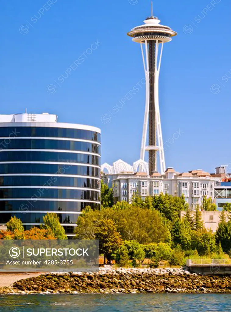 Space Needle and buildings at water's edge with trees and blue sky in Seattle, WA