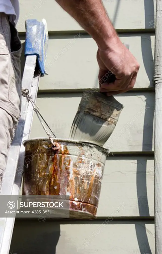 Painter wiping off excess paint on his brush while working on a wall of a Victorian house in Swampscott, MA. MR & PR