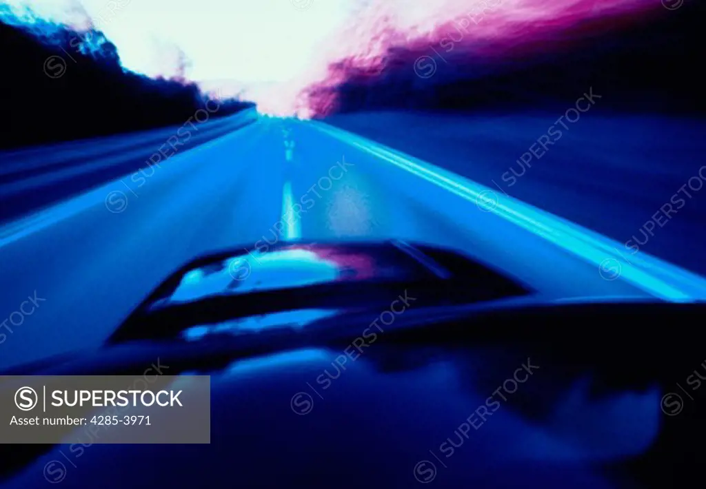 View from the hood of a car traveling on a straight two-lane road, with blurred effect to show motion.