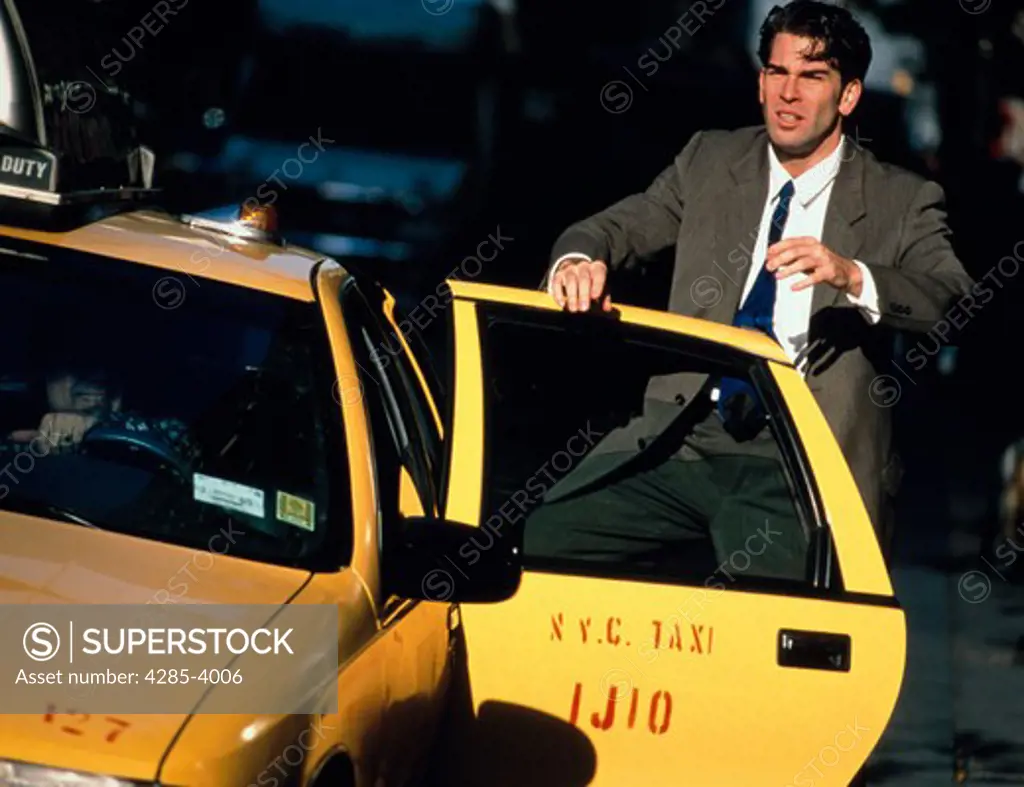 Businessman looking stressed as he gets out of a taxicab on a busy city street in New York City.