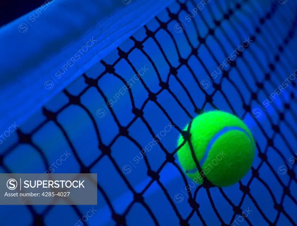 Yellow tennis ball stuck in a tennis court net.