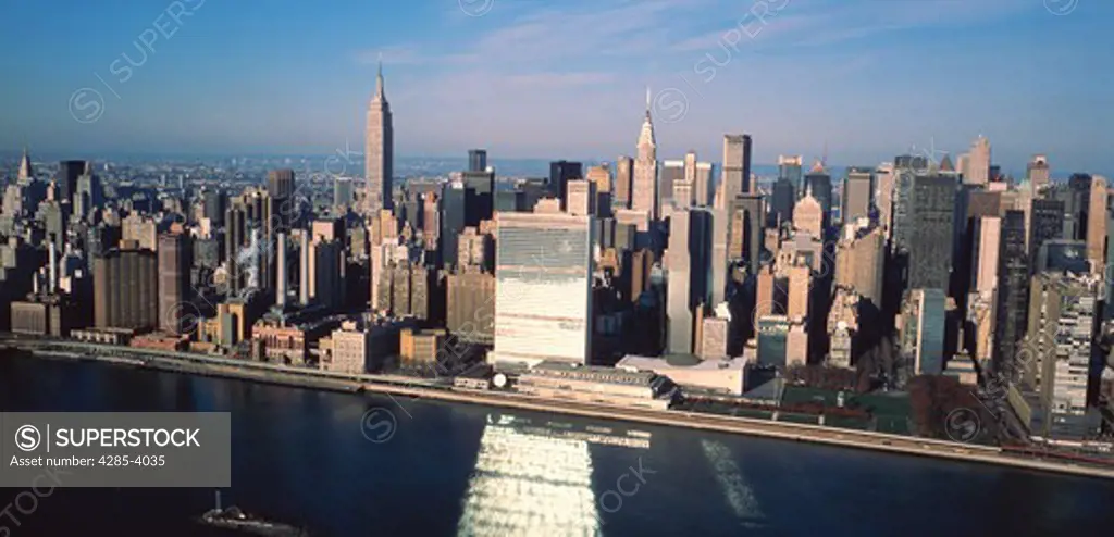 Aerial view of midtown Manhattan including the Empire State and Chrysler buildings. The UN building reflects on the East River.