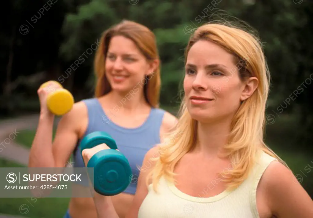 Two women excerising with weights outdoors.