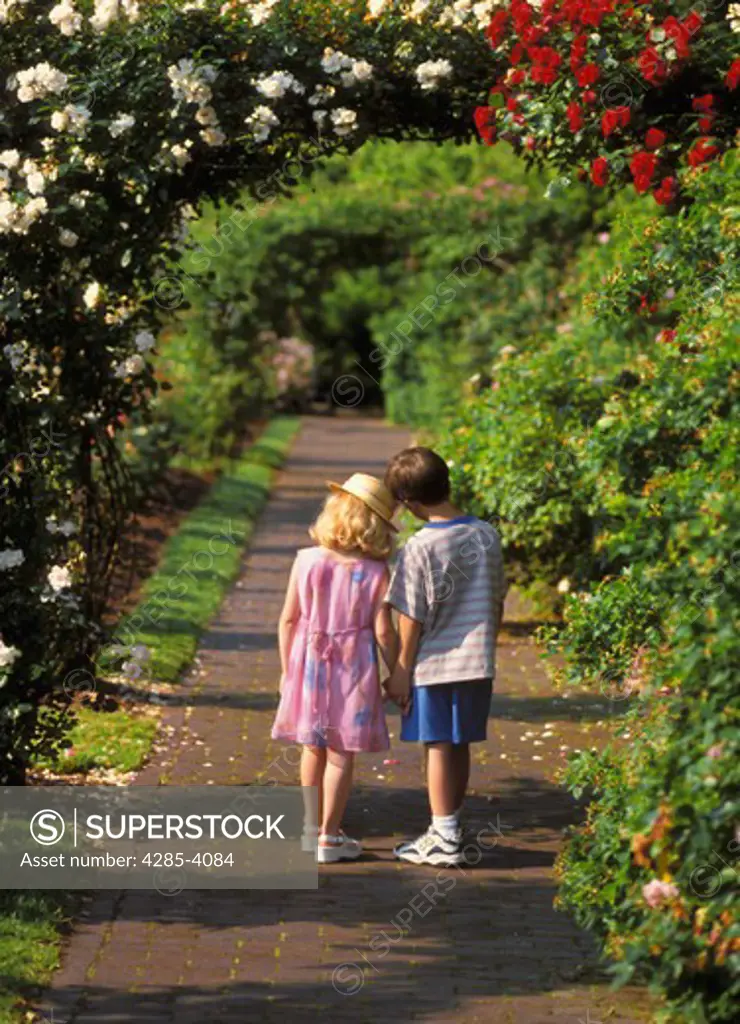 Young girl and boy standing and talking in a garden.