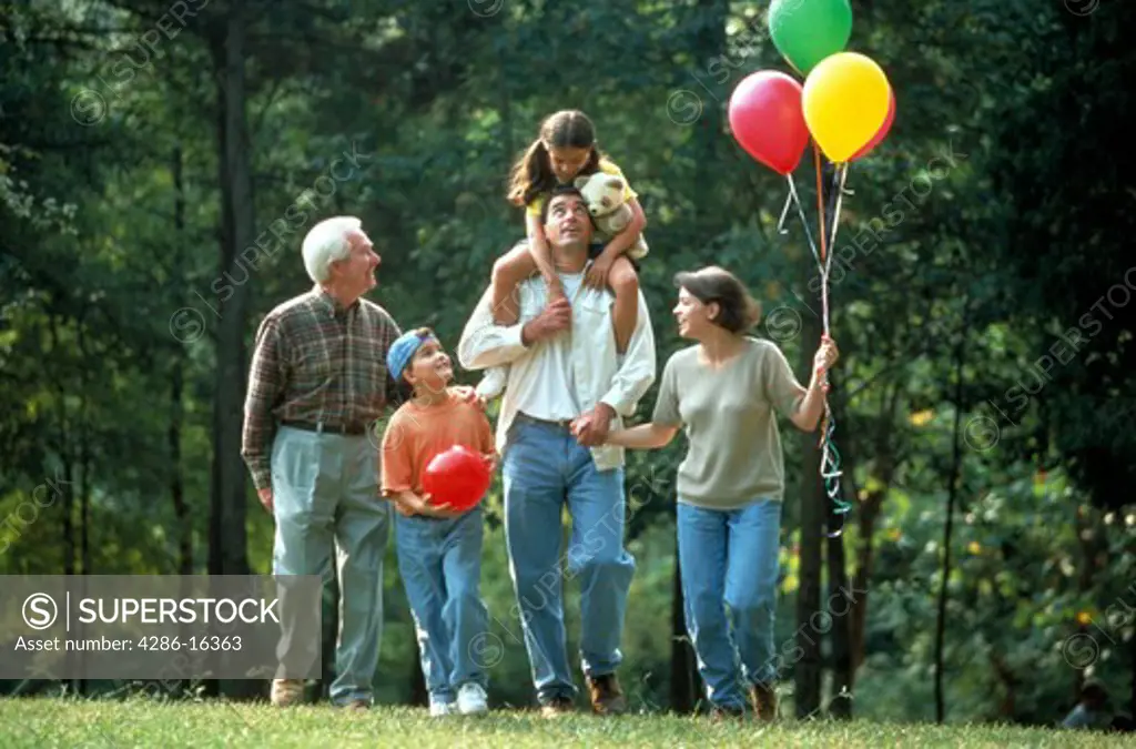 Three generations of a family with grandfather, parents and three children walking in the park with balloons.