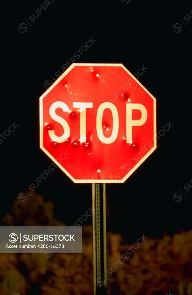 Stop sign with bullet holes scattered across it.