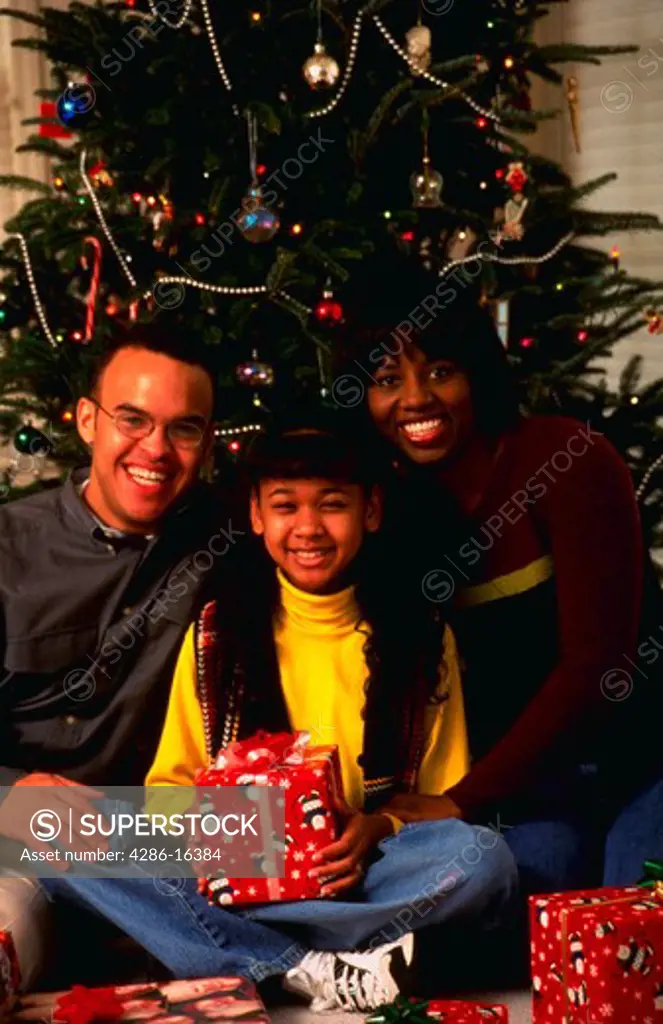 Portrait of an African American family with parents and daughter in front of a Christmas Tree.