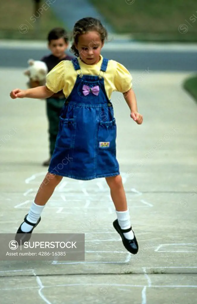 Young girl jumping in the air while playing hopscotch.