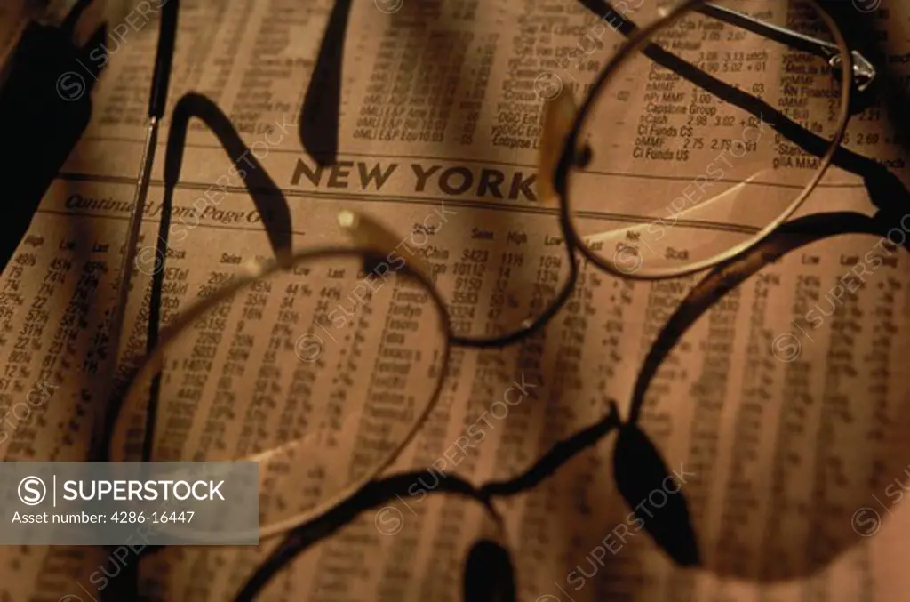 Still life of a pair of eyeglasses laying on the stock listings from a newspaper.