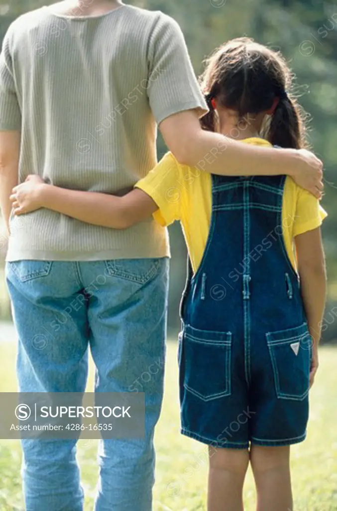 View from behind a young girl with her arm around her mothers waist while her mother¡s arm is around her shoulders.