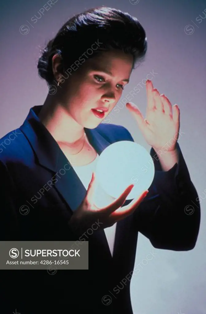 A business woman gazes into a glowing ball that she is holding as if to see the future.