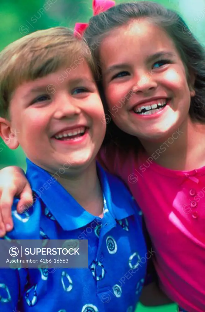 A young boy and girl smile as they stand next to each other with their arms around each other¡s shoulders.
