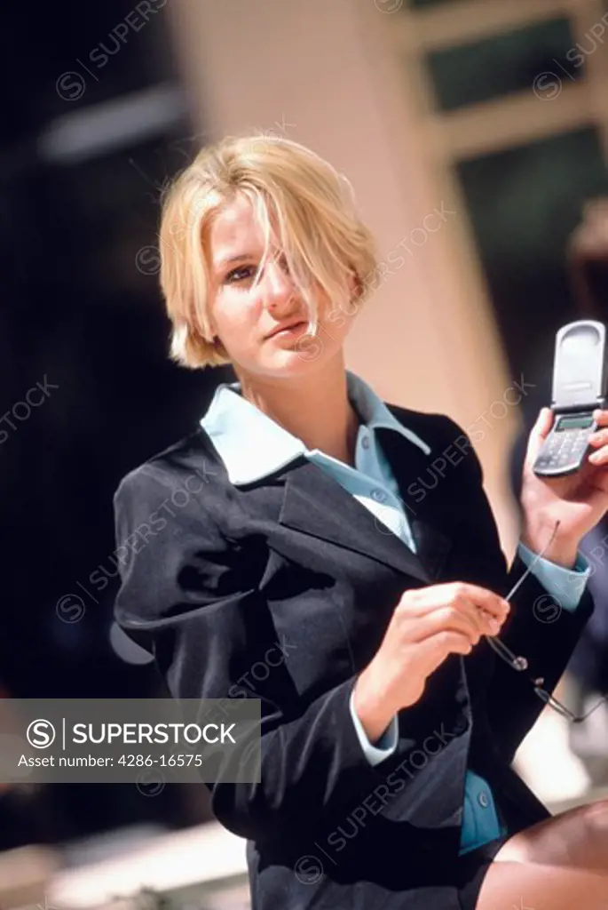 Portrait of a blonde female executive sitting outside holding her glasses and a cellular phone.
