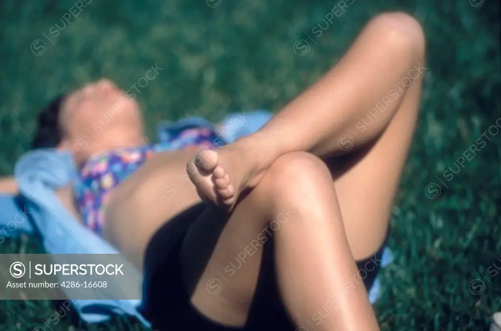 A woman with her foot propped up on her knee laying in the grass.