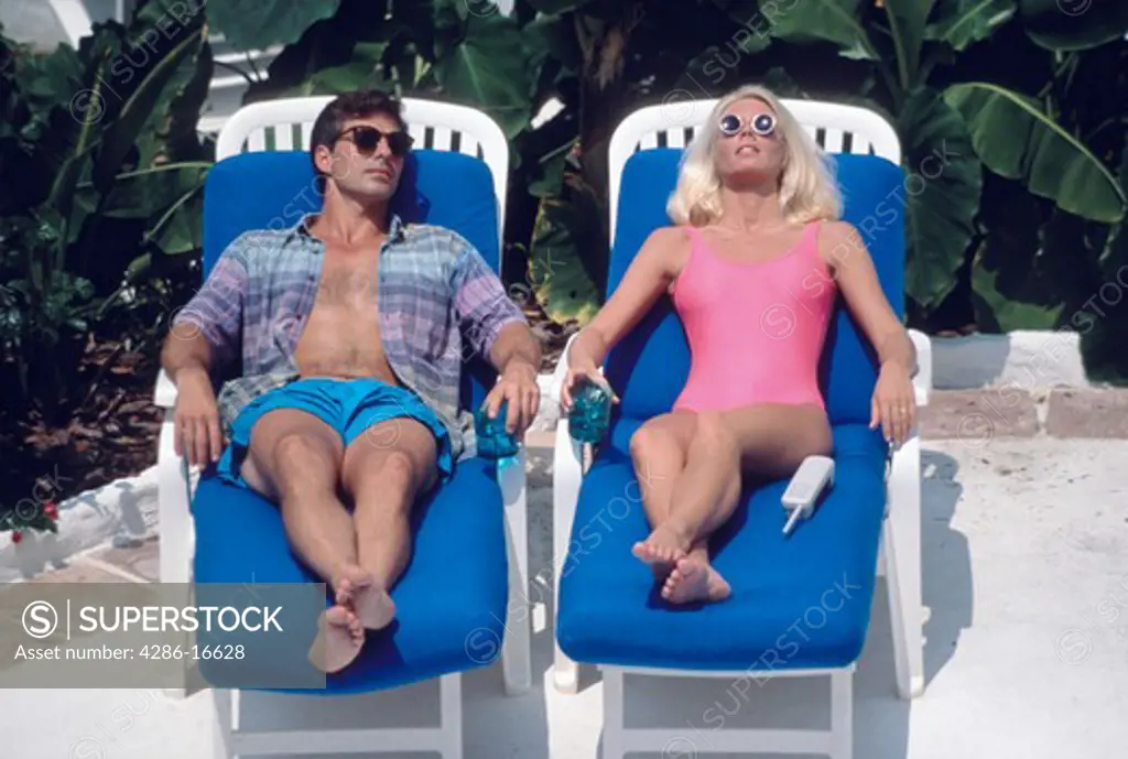 A man and a woman relaxing outside on lounge chairs.