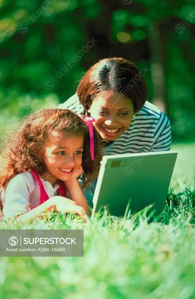 An African-American mother and daughter outside on a laptop computer.