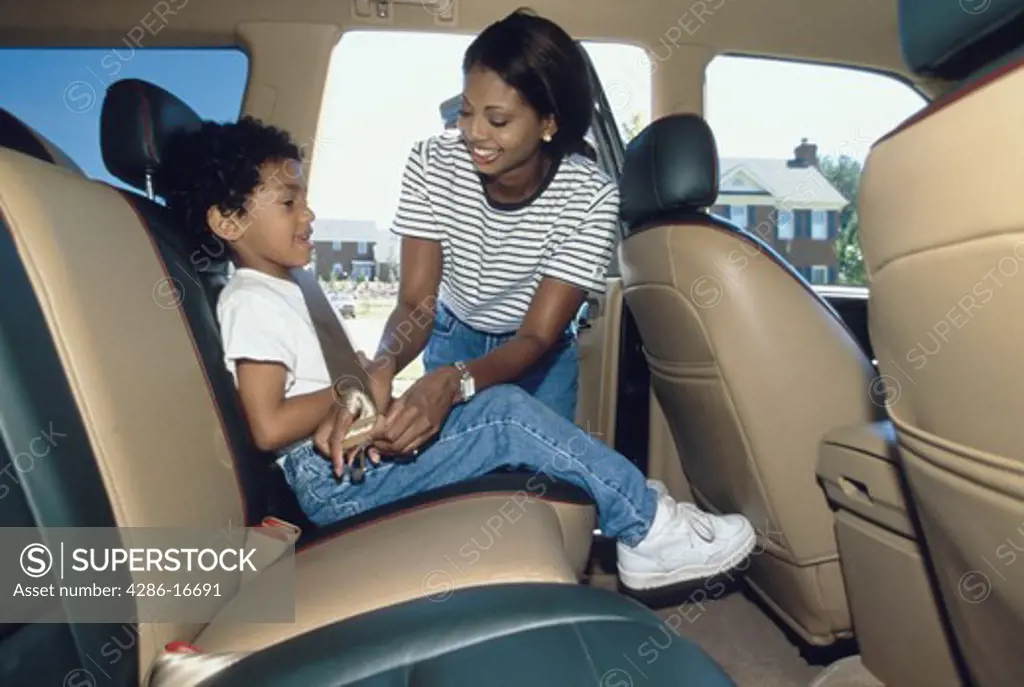 An African-American mother securing her son in a seat belt in the back seat of the auto.