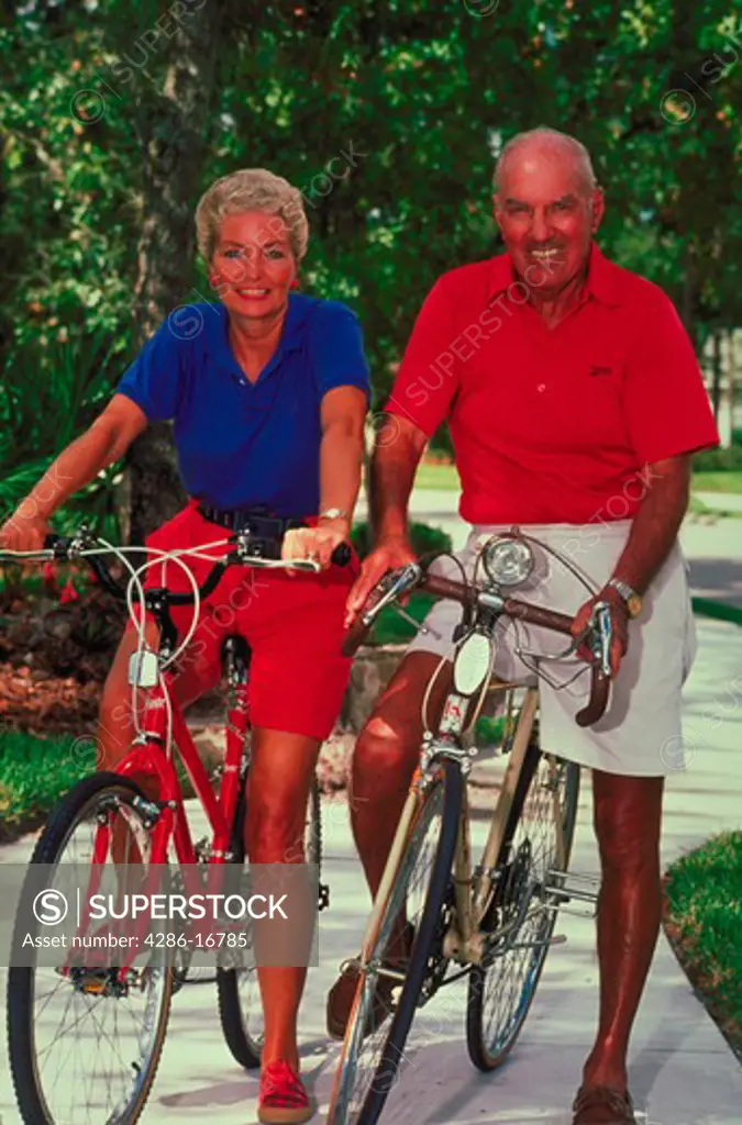 Portrait of a senior couple sitting on their bicycles in the middle of the sidewalk.