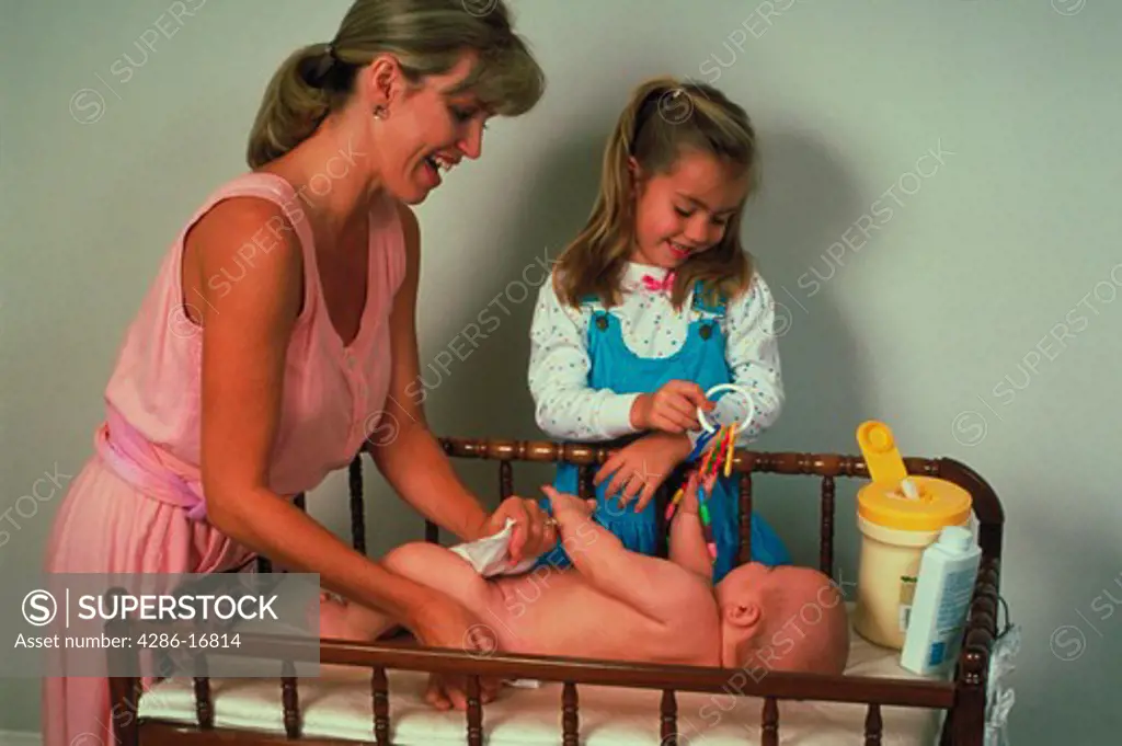 A mother changing a babys diaper while her daughter looks on.