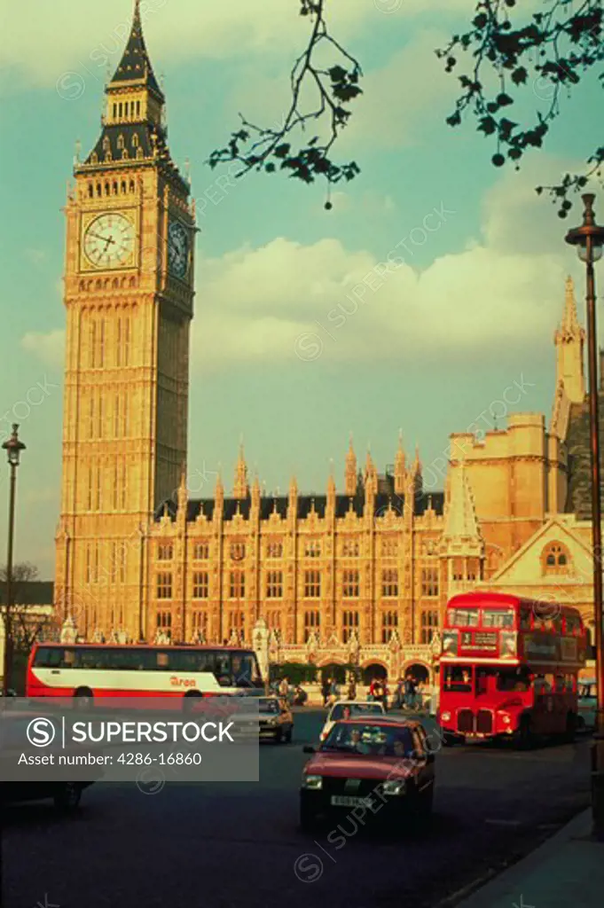 View of cars and double-decker buses in front of the Parliament building and the Big Ben clock tower in London, England.