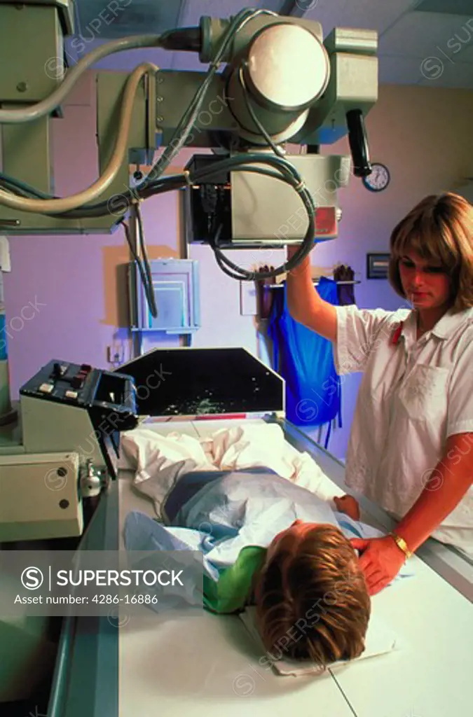 A female medical technician preparing to give an x-ray to a child who is laying on a table.