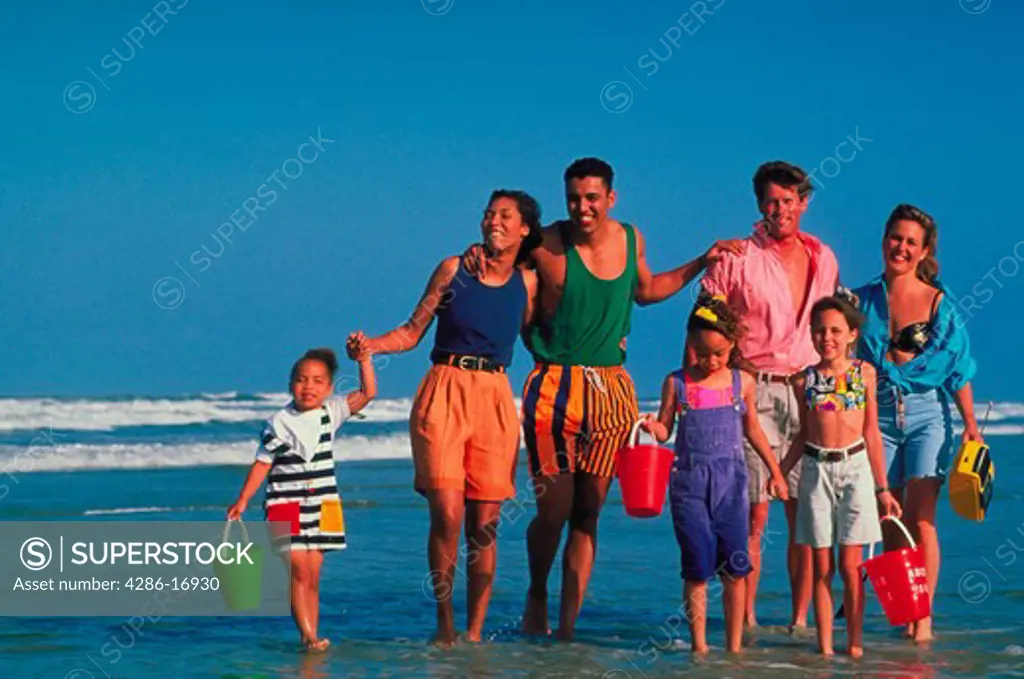 Two families walking through the surf together carrying sand pales and a radio.