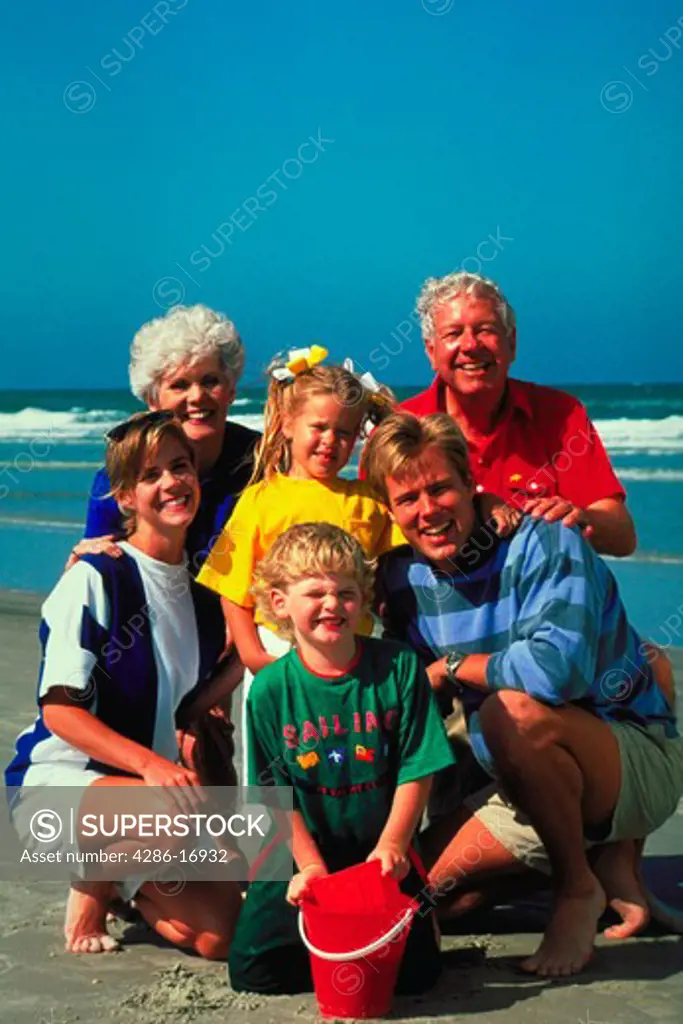 Portrait of three generations of a family on the beach with the surf in the background.
