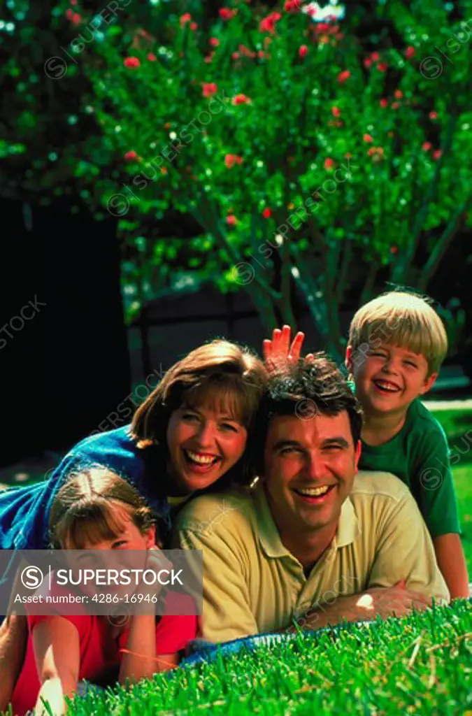 Portrait of a smiling Mother, Father and two children lying in the grass.