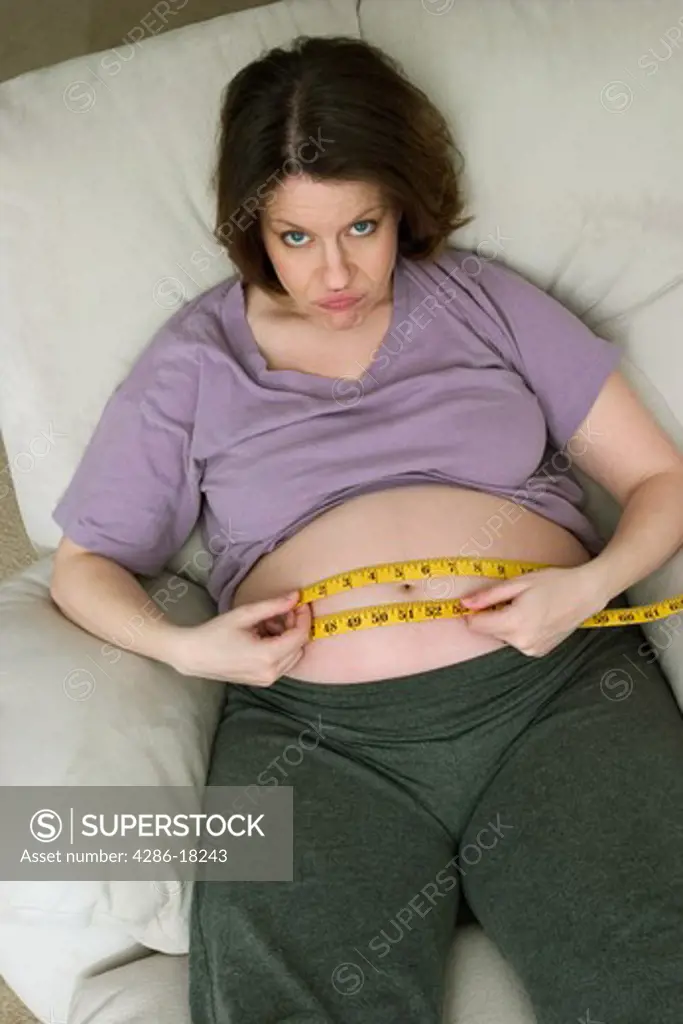 Pregnant woman, sitting on a chair, measuring her belly with a tape measure.  MODEL RELEASED.