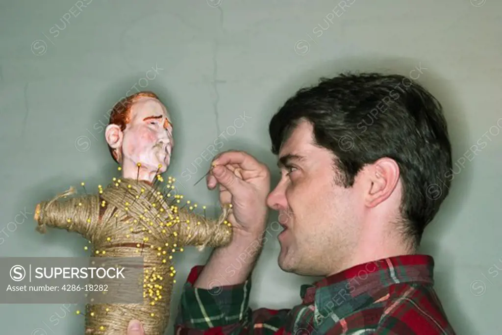 Young male artist sticking a pin into a voodoo doll.  MODEL RELEASED.