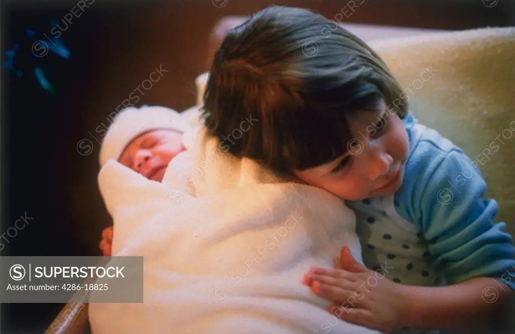 Three-year-old girl holding and hugging newborn baby wrapped in a blanket.