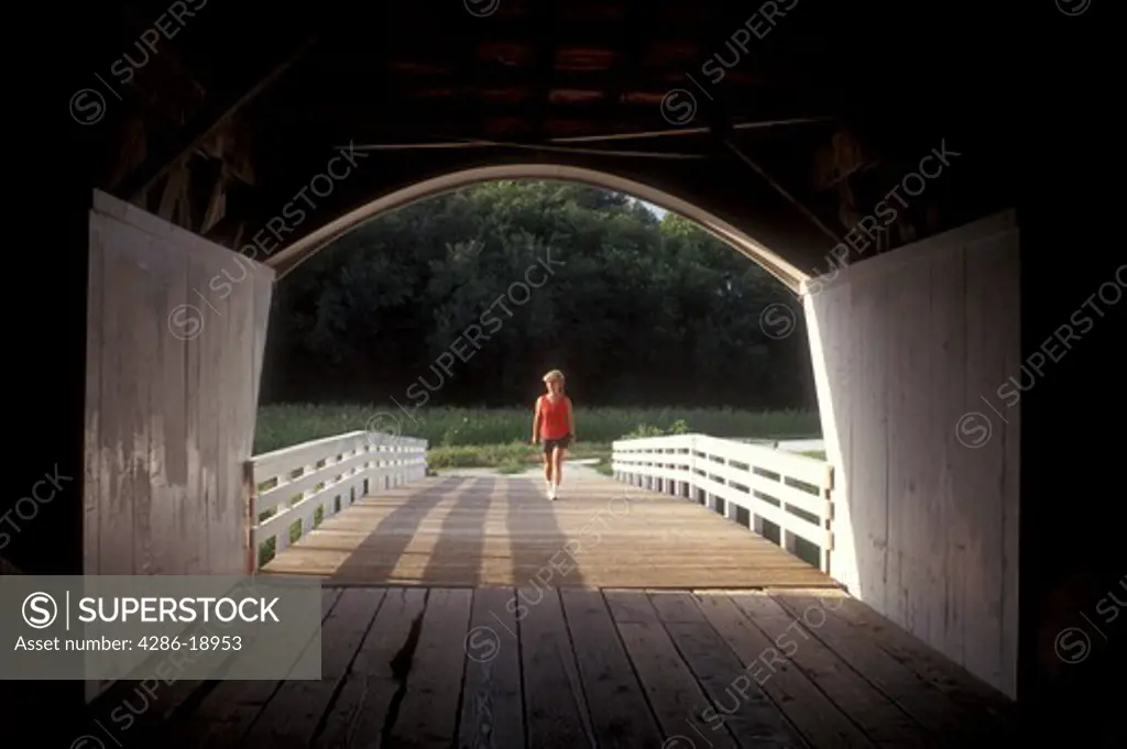 Iowa, Winterset, covered bridge, Woman walking towards circa 1883 Roseman Covered Bridge in Winterset.Bridges of Madison County.
