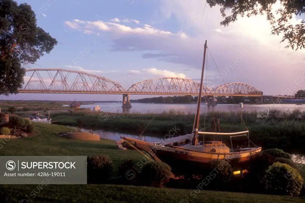 North Dakota, Bismarck, A sailboat is beached on the shoreline of the Missouri River in the early evening in Bismarck. A bridge spans the river in the background.