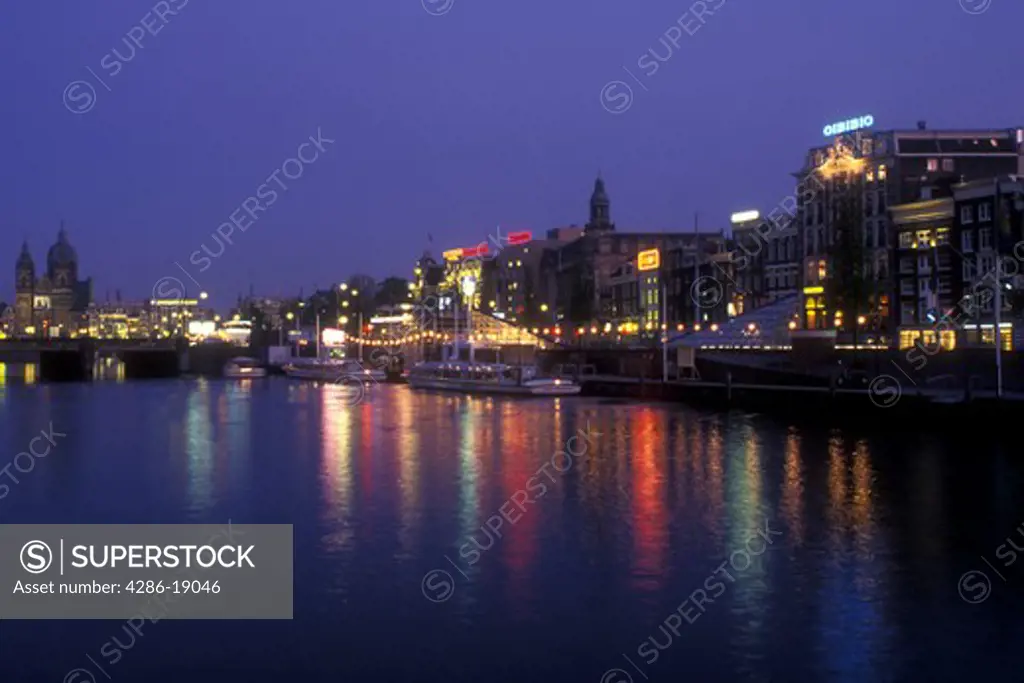 Netherlands, Amsterdam, The lights of Open Haven Front in downtown Amsterdam reflect in the calm waters of the canal in the evening. 