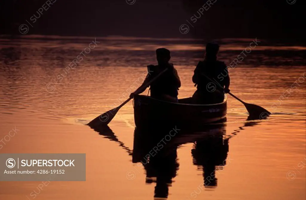 Vermont, canoe, canoeing, Mother and daughter paddle a canoe over the quiet calm waters of Kettle Pond atsunrise, sunset in Groton State Forest. Mad River Canoe Products.