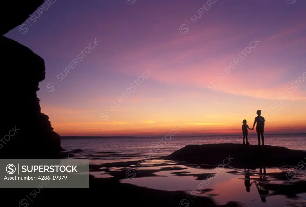 Pictured Rocks, Lake Superior, silhouette, sunset, sunrise, Upper Peninsula, U.P., Michigan, Mother and daughter standing holding hands on the edge of Lake Superior at sunset at Pictured Rocks National Lakeshore in Munising in the state of Michigan.