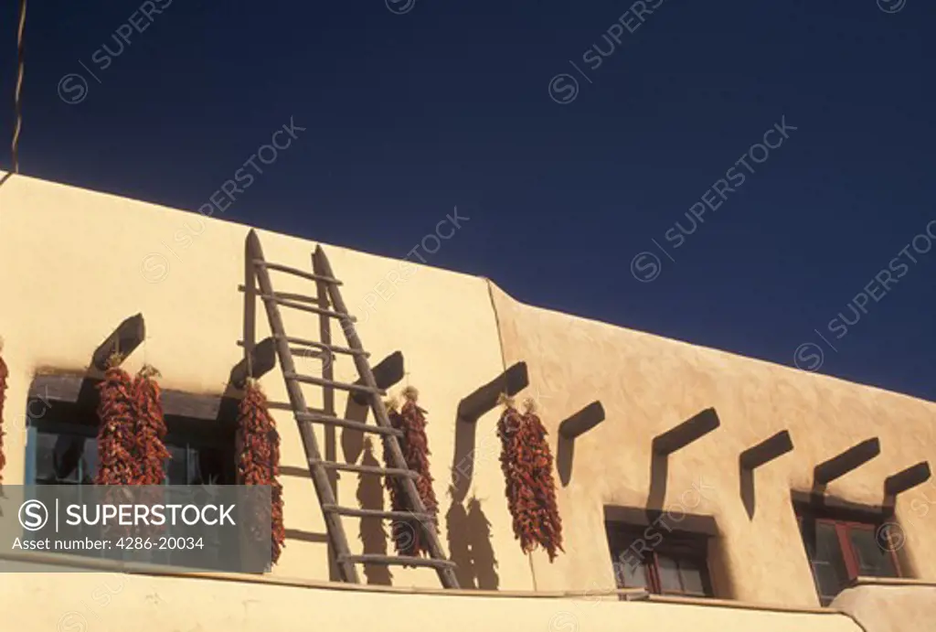 Taos, NM, New Mexico, Clusters of chili peppers drying outside an adobe style building in the village of Taos.