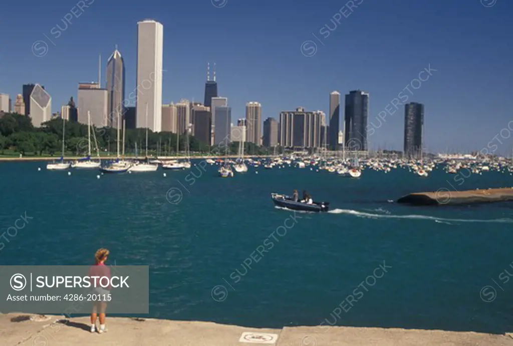 Chicago, IL, Illinois, Lake Michigan, skyline, Woman watching a boat in the Chicago Harbor from Grant Park with a view of the downtown skyline of Chicago. 